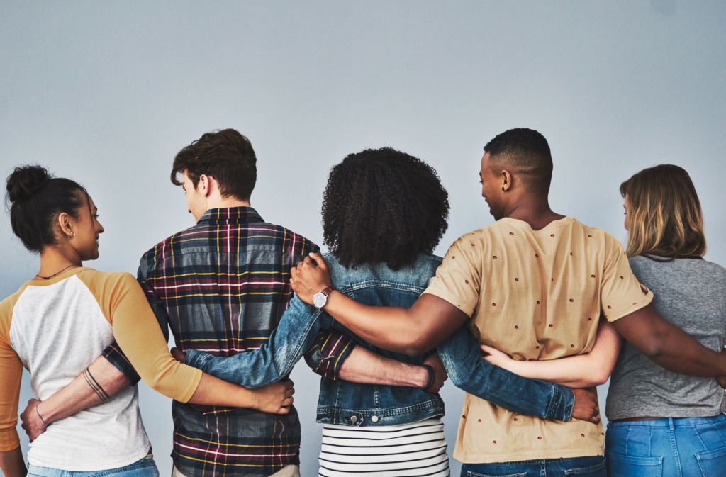 Rearview studio shot of a diverse group of young people embracing each other against a gray background