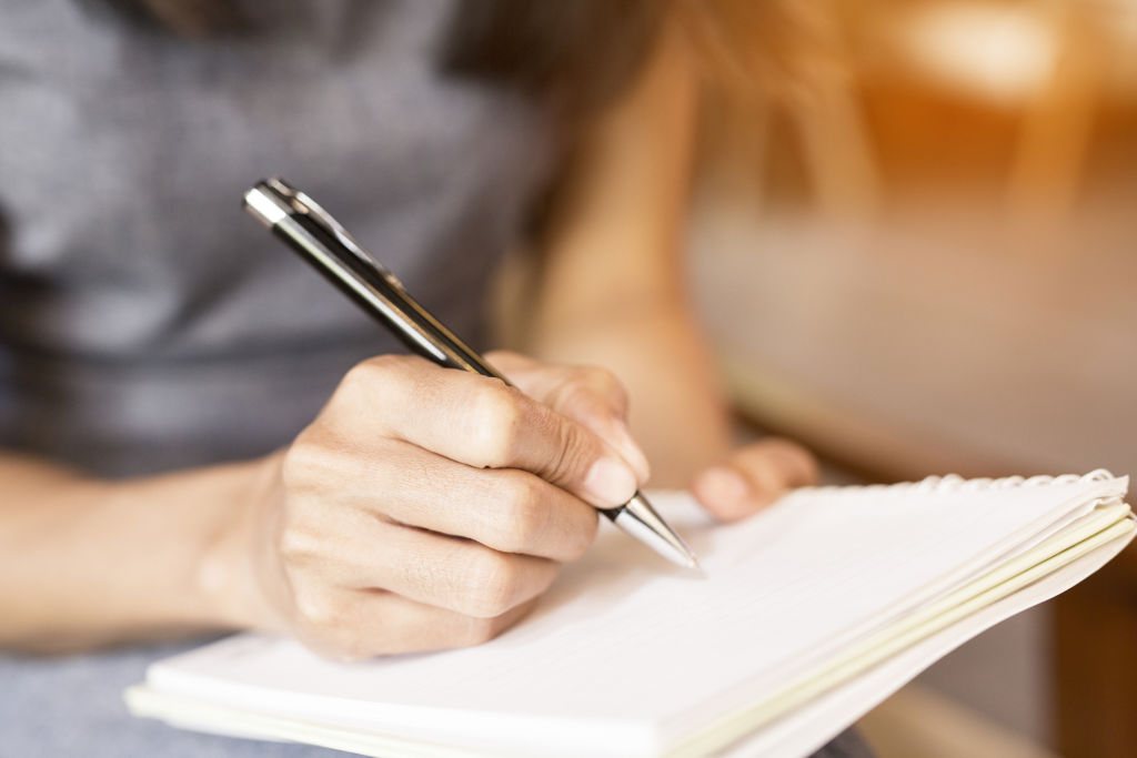 Women holding a pen while writing in a notebook.