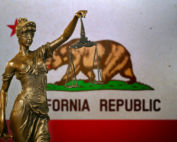 Close-up of a small bronze statuette of Lady Justice before a flag of California.