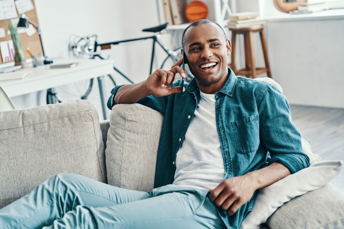 Handsome young African man talking on the smart phone and smiling while sitting indoors