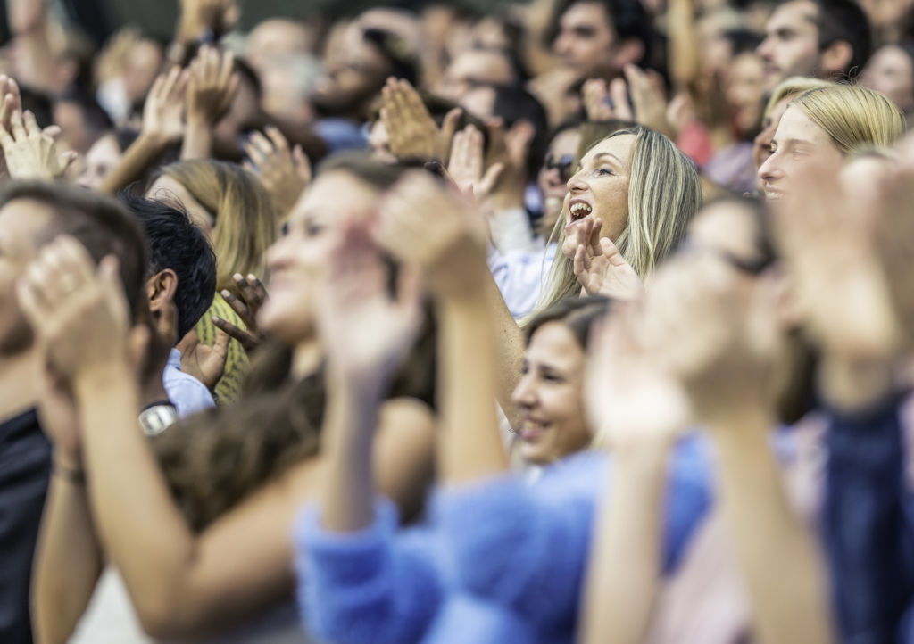 Large group of people on a stadium cheering and clapping during a sports match.